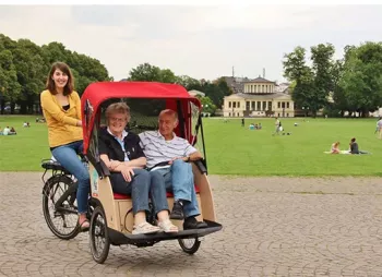 Natalie Chirchiette vom Verein Radeln ohne Alter fährt mit einer Rikscha ein älteres Paar durch Bonn.